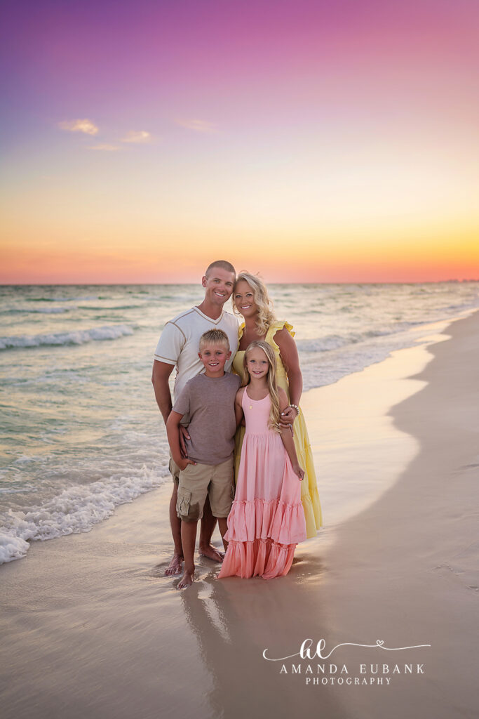 Parents pose with their kids on the Destin sand as the sky turns pink behind them