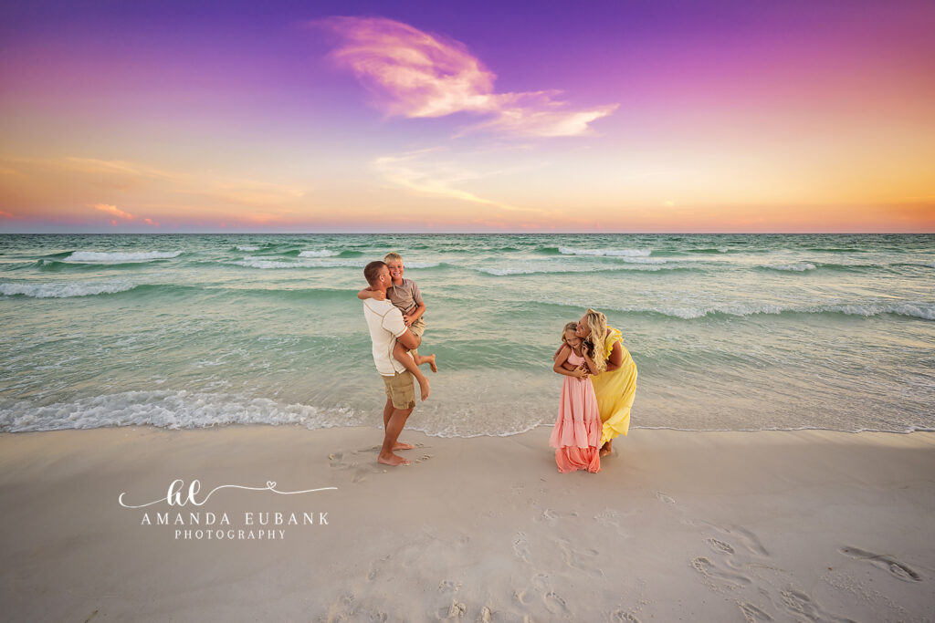 Mom and Dad share a hug as their daughters play at the water edge during a Destin sunset session