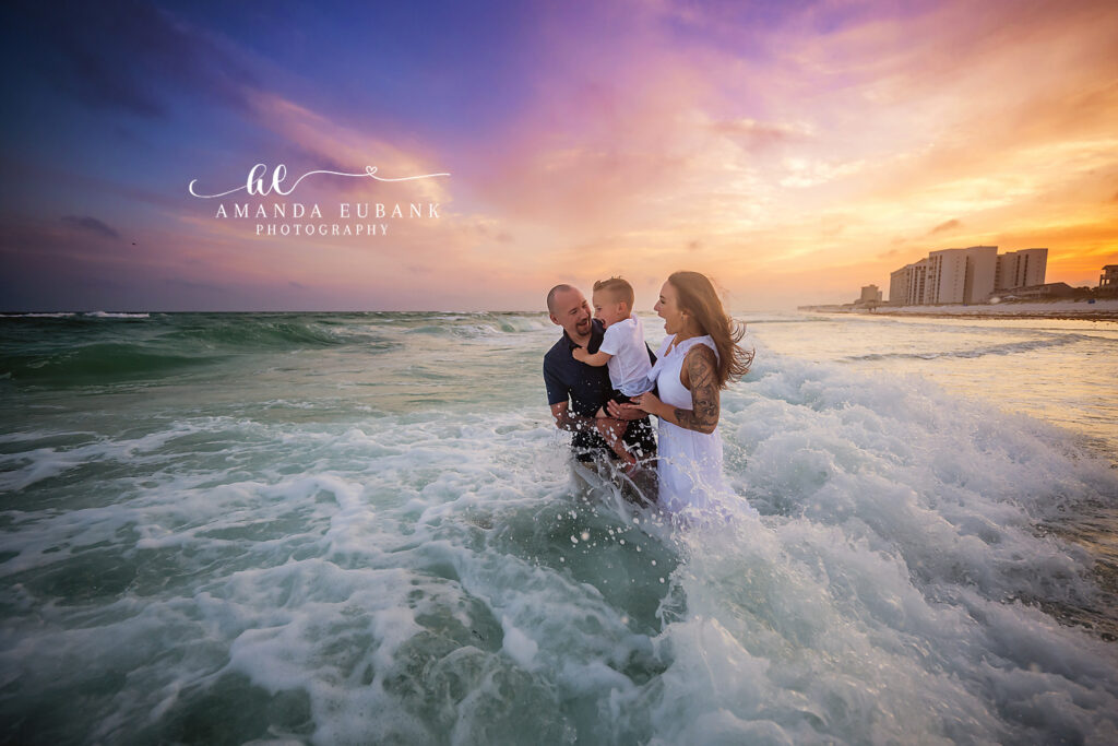 M family laughing together in the splashing waves at Destin sunset