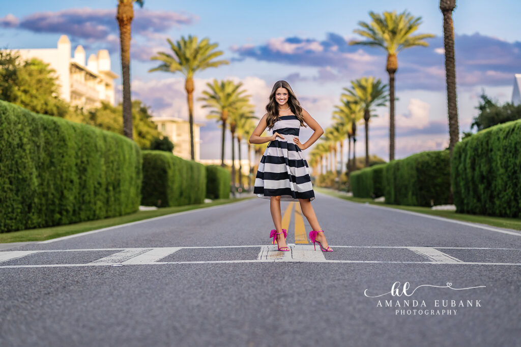 Sunset senior portrait of Miss L glancing back along the cobblestone street as palm shadows stretch out in Alys Beach, FL.