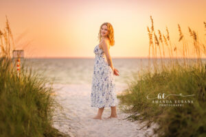 Sunset senior portrait of Miss C in a floral dress, walking the soft white sand at the water's edge in Rosemary Beach, FL.