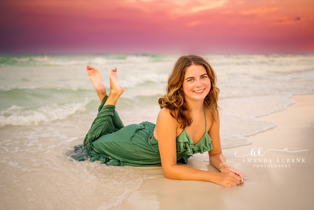 Senior Miss A in a forest green flowy dress with sunset glow on her shoulders at the 30A shoreline.