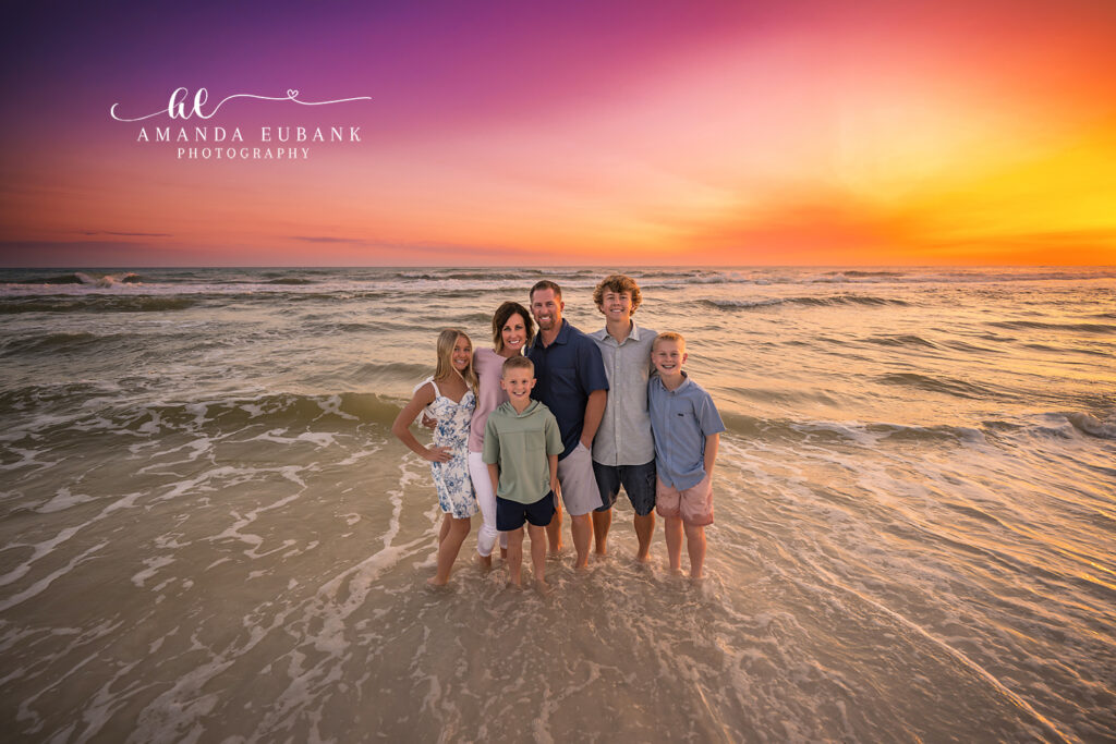 Dune Allen sunset family photographer captures six in the foamy surf under a fuchsia and gold sunset.