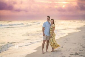 Newly engaged couple final sunset portrait on Carillon Beach, fiance in blue polo, fiancee in yellow floral maxi dress.