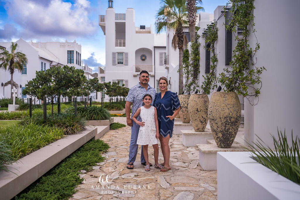 Alys Beach sunset family photographer captures the trio on stone pavers in the pottery plaza with the white tower behind.