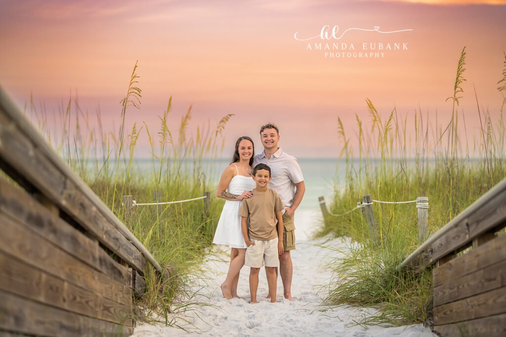Destin family beach sunset photographer captures three smiling on the wooden boardwalk in coordinated linen attire.