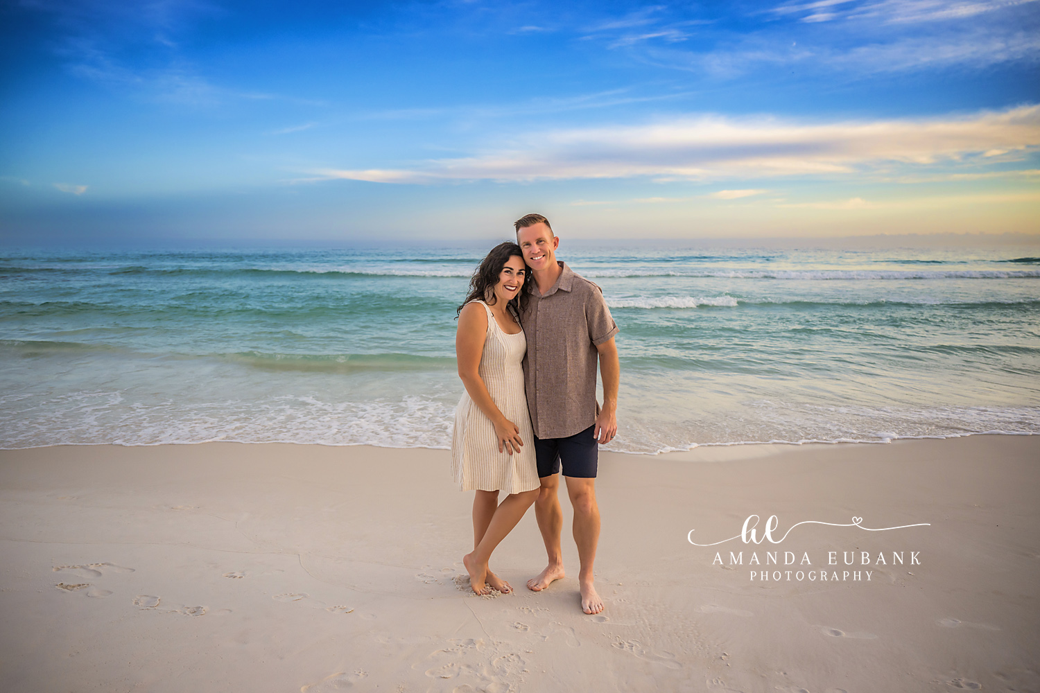 Destin Couple Beach Portrait at Henderson Beach State Park | Destin FL Family Photographer Husband and wife in cream and sage coastal outfits standing arm in arm on the white sand at Henderson Beach State Park in Destin FL with the Gulf and a blue sky