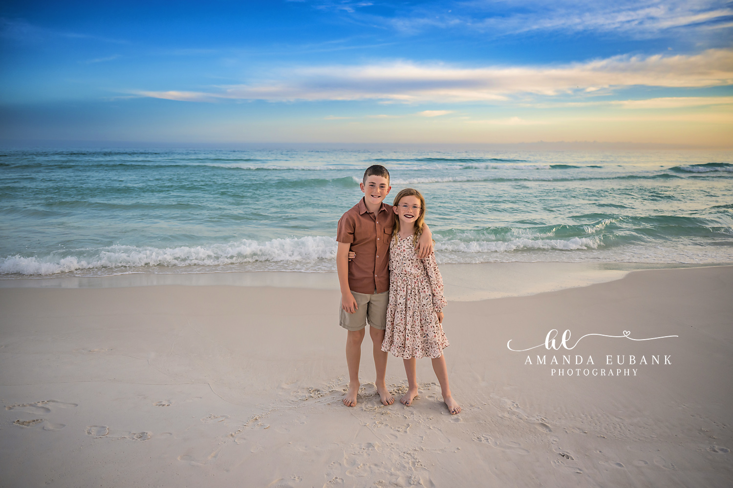 Destin Brother and Sister Beach Portrait | Destin FL Family Photographer Brother in a rust polo with arm around his sister in a floral dress on the white sand at Henderson Beach State Park in Destin FL with the turquoise Gulf behind them