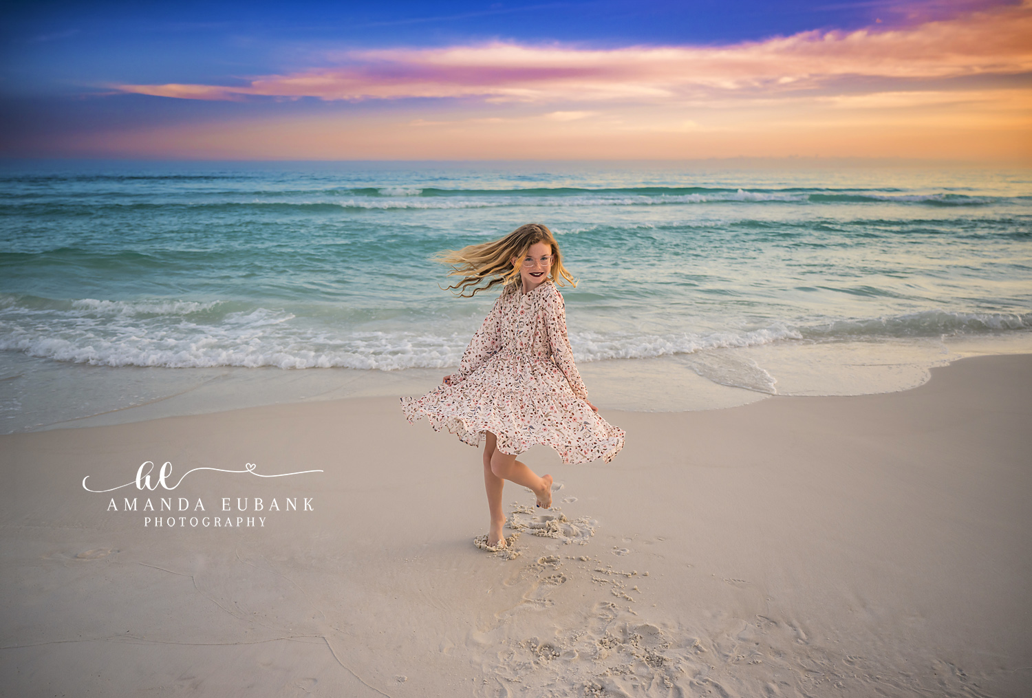 Destin Sunset Twirl Daughter Beach Portrait | Destin FL Family Photographer Young girl with red hair twirling in a floral dress on the Destin FL shoreline at sunset with the Gulf surf and a pink and orange sky behind her
