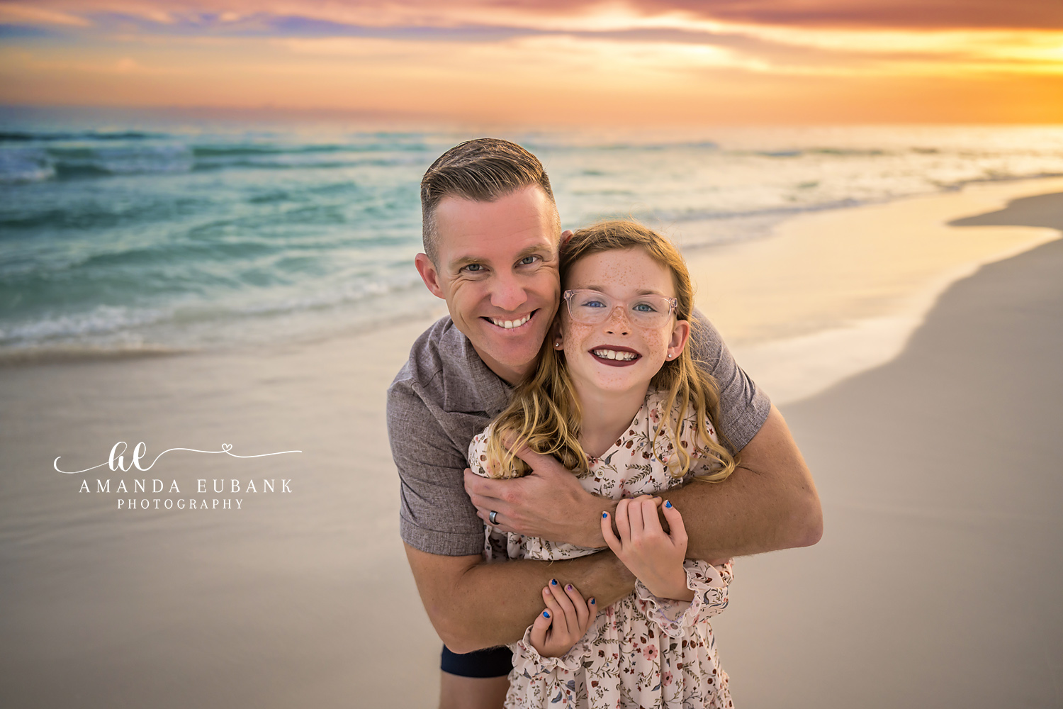 Destin Father Daughter Sunset Hug Portrait | Destin FL Family Photographer Dad hugging his red haired daughter from behind both smiling on Destin FL beach at sunset with the Gulf and golden sunset light behind them