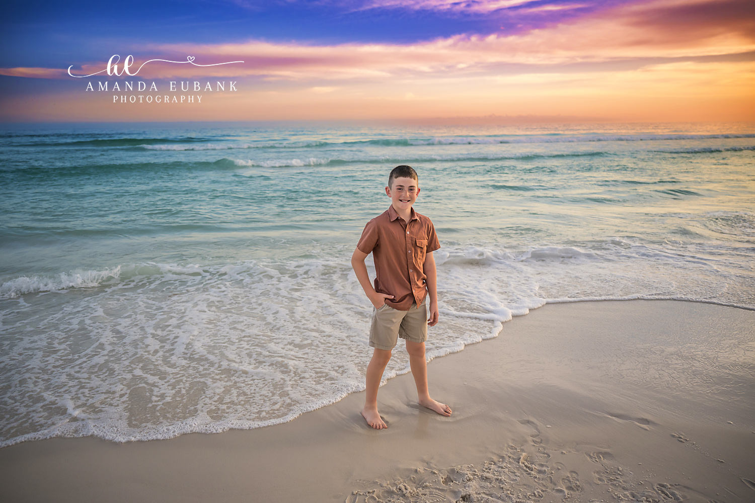 Destin Son Sunset Beach Solo Portrait | Destin FL Family Photographer Boy in a rust polo and cream shorts standing with hand on hip on the Destin FL shoreline at sunset with the Gulf surf and a pink and orange sky behind him