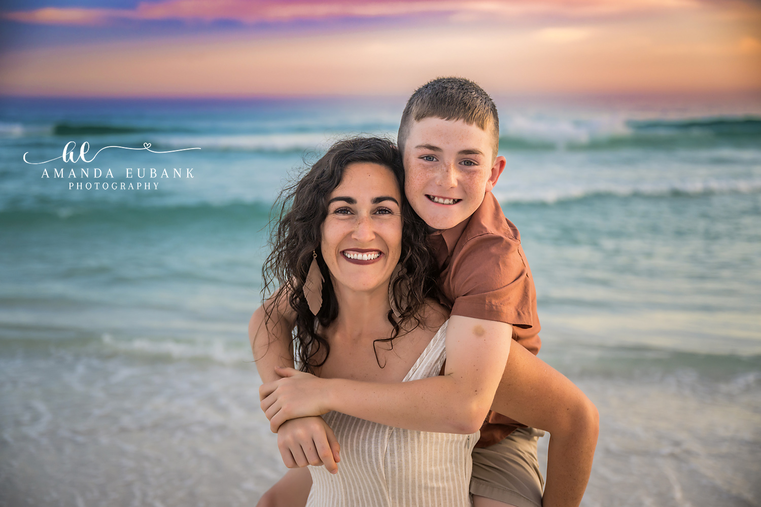 Destin Mom and Son Piggyback Sunset Portrait | Destin FL Family Photographer Mom giving her son a piggyback ride both grinning on the Destin FL beach at sunset with the Gulf and a pastel sky behind them
