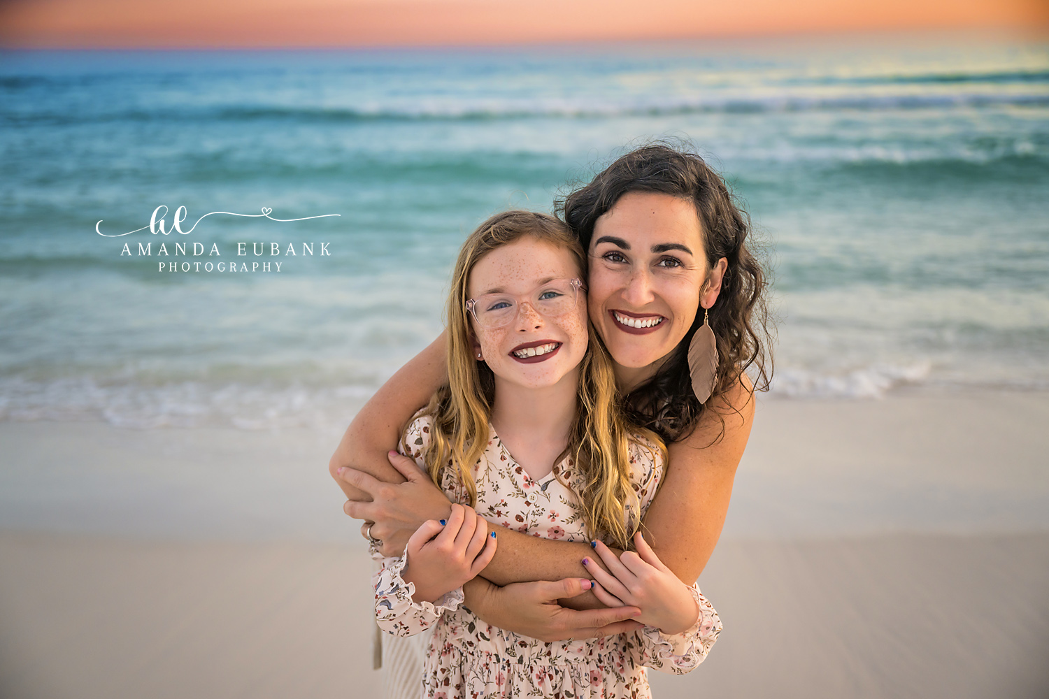 Destin Mother and Daughter Sunset Hug Portrait | Destin FL Family Photographer Mom hugging her freckled red haired daughter from behind both beaming on the Destin FL beach at sunset with the Gulf and a soft pastel sky