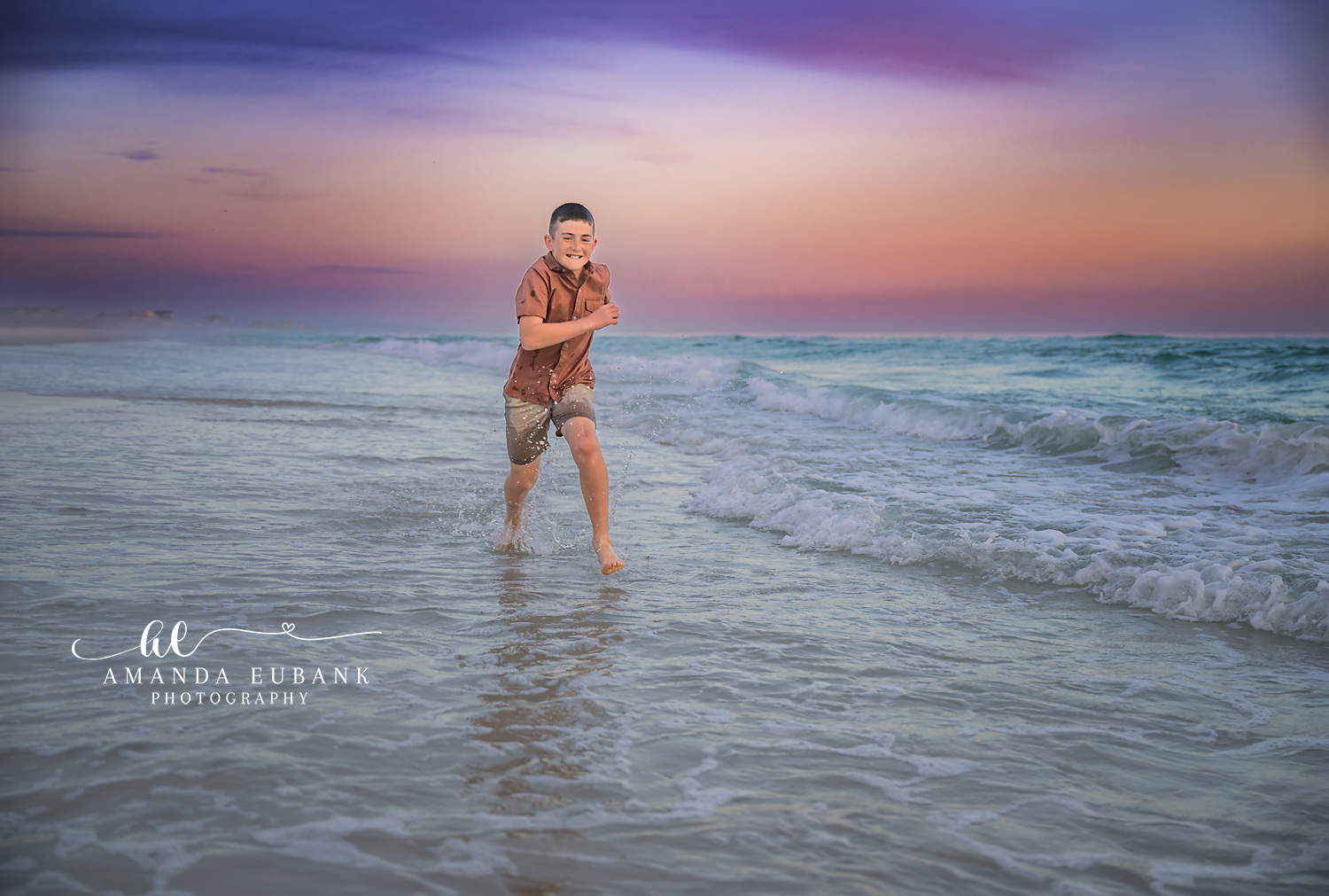 Destin Son Running Through the Surf Sunset Portrait | Destin FL Family Photographer Boy in a rust polo running and splashing through the foamy Gulf surf at Destin FL at sunset with a pastel pink and lavender sky