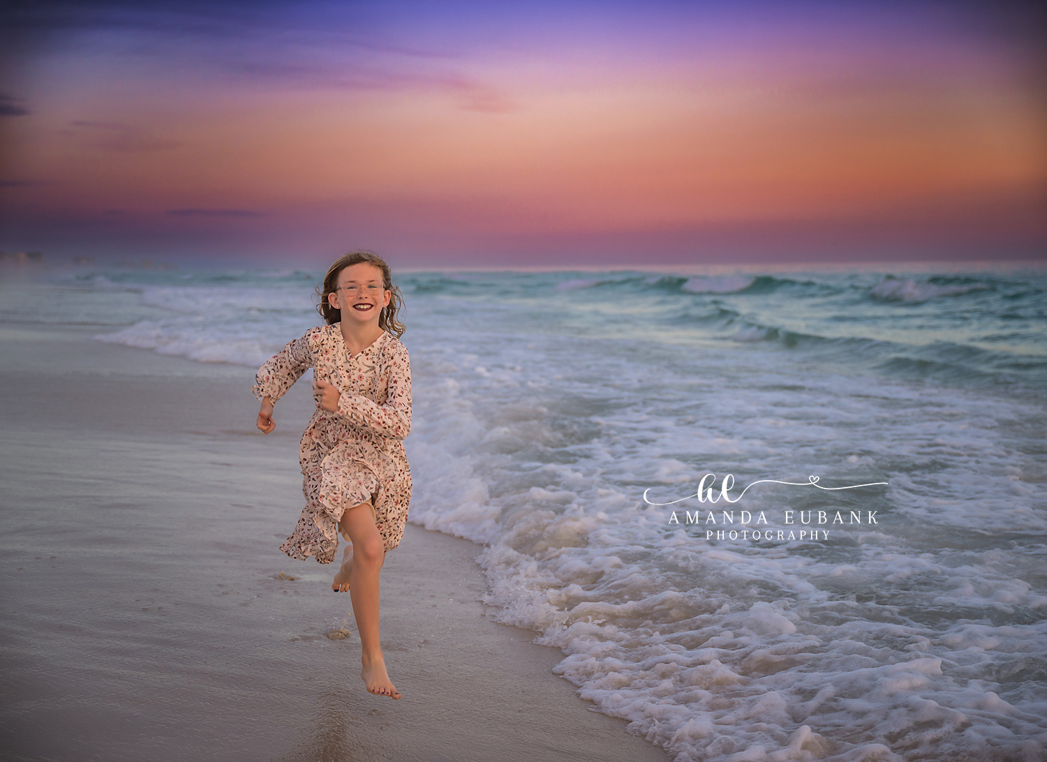 Destin Daughter Running Through the Surf Sunset Portrait | Destin FL Family Photographer Red haired girl in a floral dress running through the foamy Gulf surf at Destin FL at sunset with a soft pastel pink and lavender sky behind her