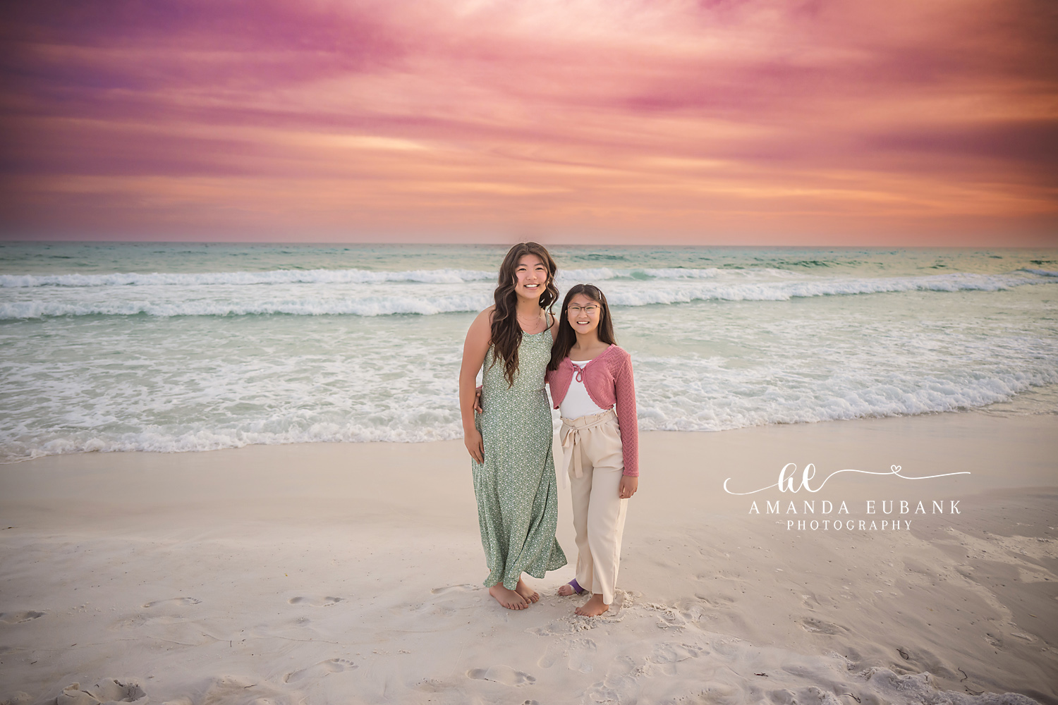Miramar Beach Mother and Daughter Sunset Portrait | Miramar Beach FL Family Photographer Mother in sage green floral maxi dress and daughter in pink cardigan and cream pants on Miramar Beach FL sand at sunset with a pastel pink sky