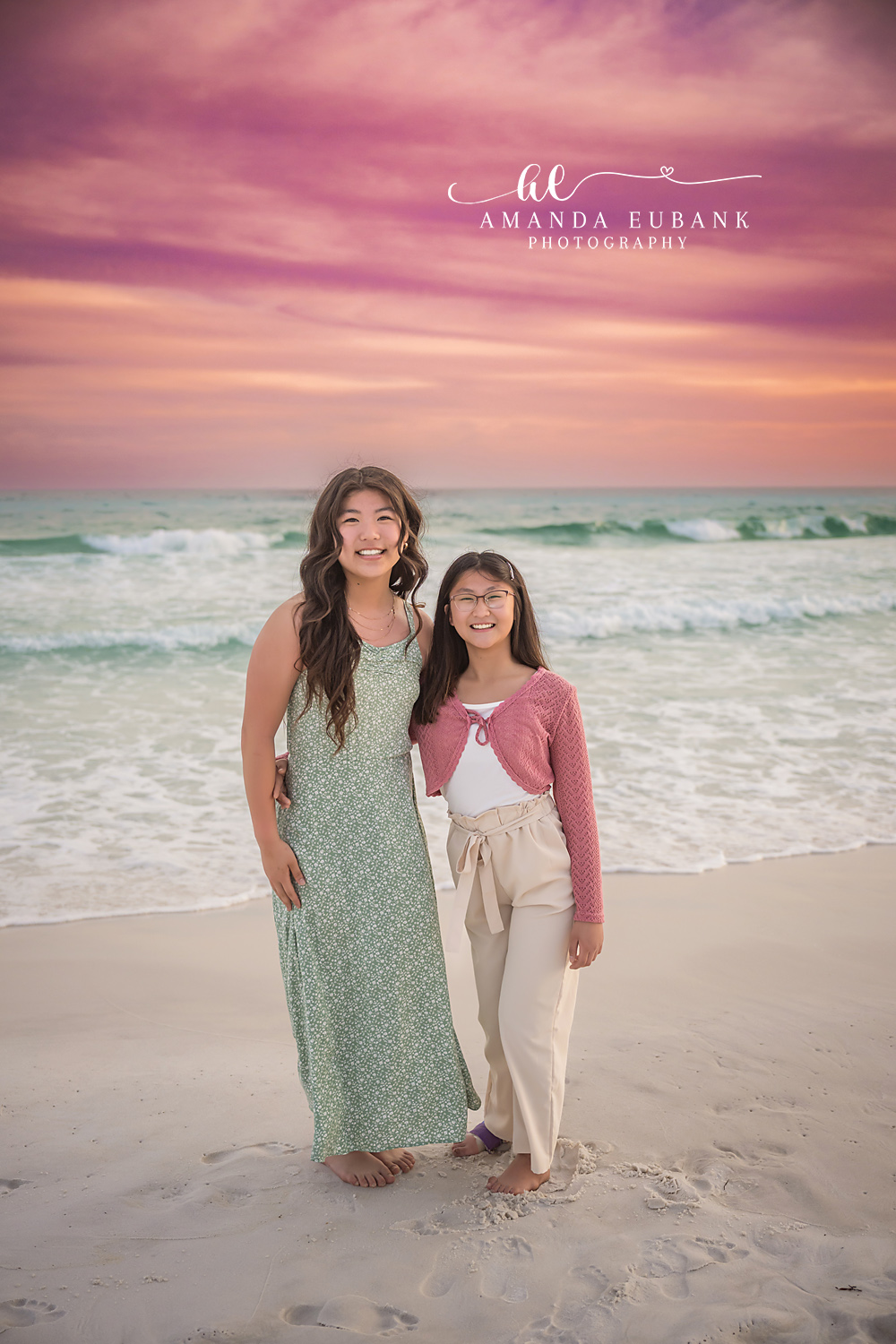 Miramar Beach Mother Daughter Sunset Smiles | Miramar Beach FL Family Photographer Smiling mother and daughter standing together on Miramar Beach FL sand at sunset with the Gulf and a pink coral sky behind them