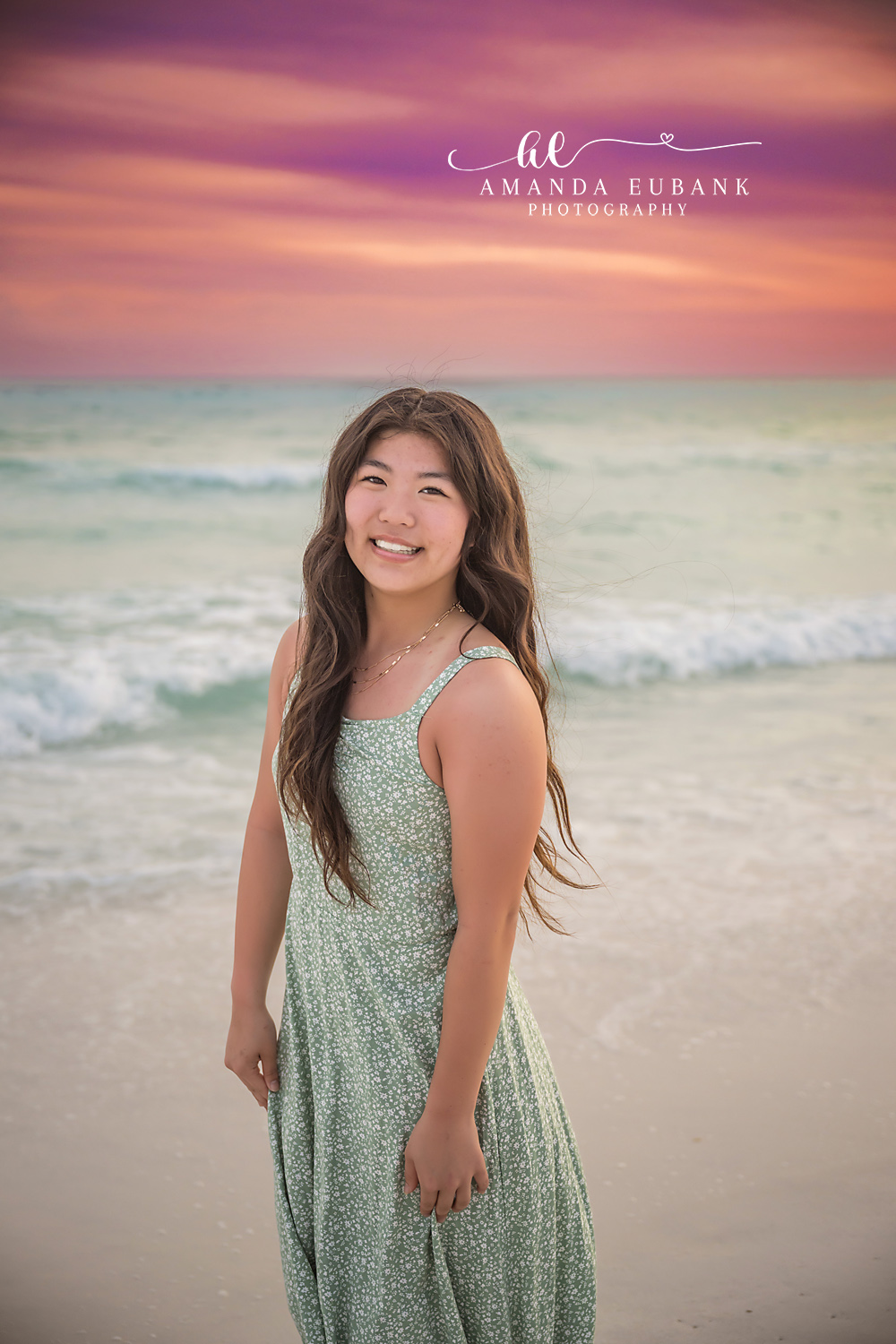 Miramar Beach Sunset Smile Portrait | Miramar Beach FL Family Photographer Smiling young woman in a sage green floral maxi dress on Miramar Beach FL at sunset with the Gulf surf and a purple pink sky behind her
