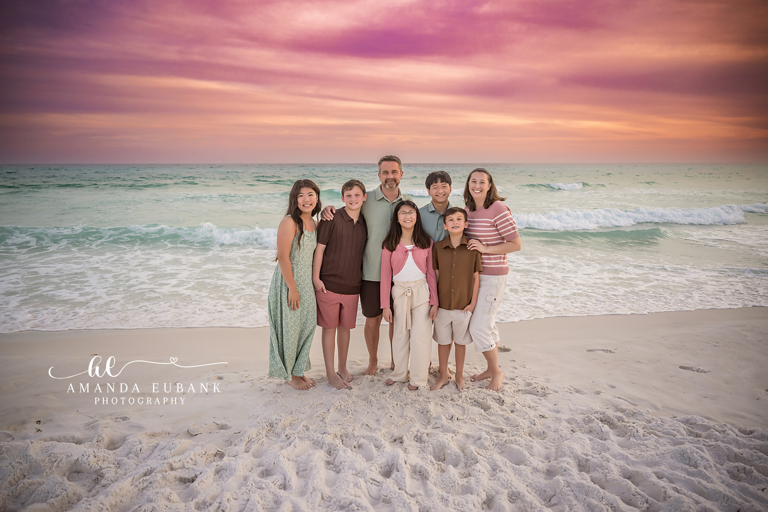 Miramar Beach Family of Seven Wide Sunset Sky Portrait | Miramar Beach FL Family Photographer Family of seven gathered together on Miramar Beach FL with the Gulf surf and a sweeping pink purple and orange sunset sky stretching across the horizon