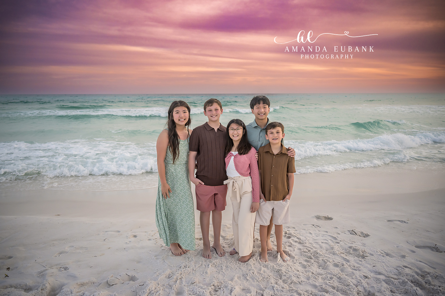 Miramar Beach Five Siblings Sunset Portrait | Miramar Beach FL Family Photographer Five siblings in coordinated sage pink coral and brown coastal outfits standing together on Miramar Beach FL at sunset with the Gulf surf and a purple pink sky