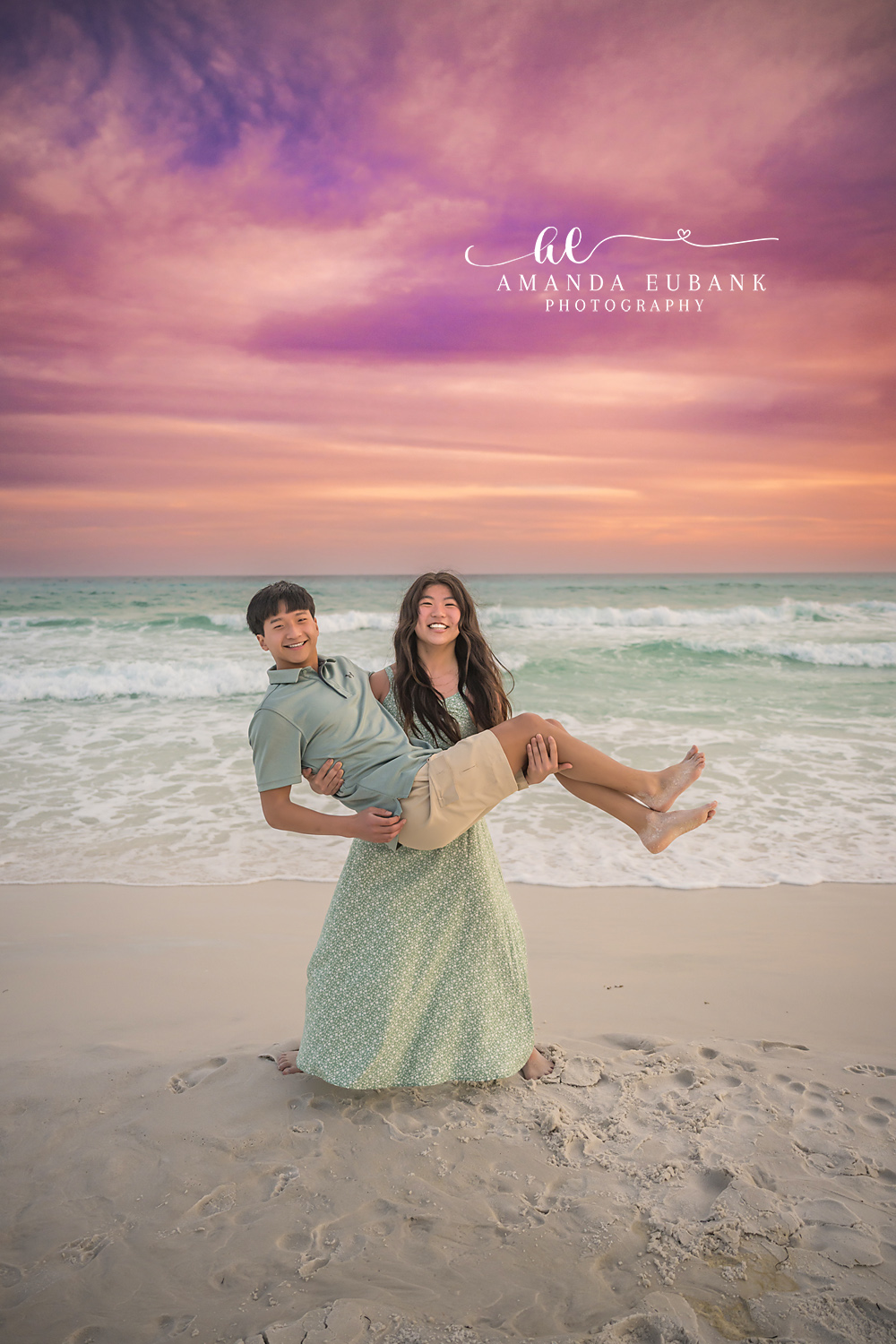 Miramar Beach Playful Siblings Sunset Portrait | Miramar Beach FL Family Photographer Older sister and her brother laughing together in a playful pose on Miramar Beach FL at sunset with the Gulf surf and a vivid pink purple sky behind