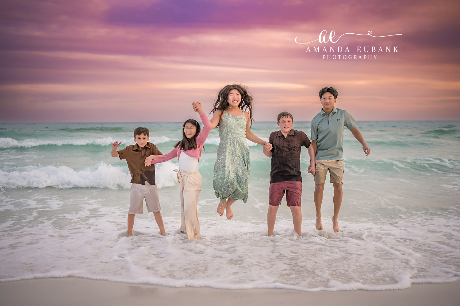 Miramar Beach Siblings Jumping in Surf Sunset Portrait | Miramar Beach FL Family Photographer Five M family siblings jumping and leaping together in the Gulf surf on Miramar Beach FL at sunset beneath a vivid pink and purple sky