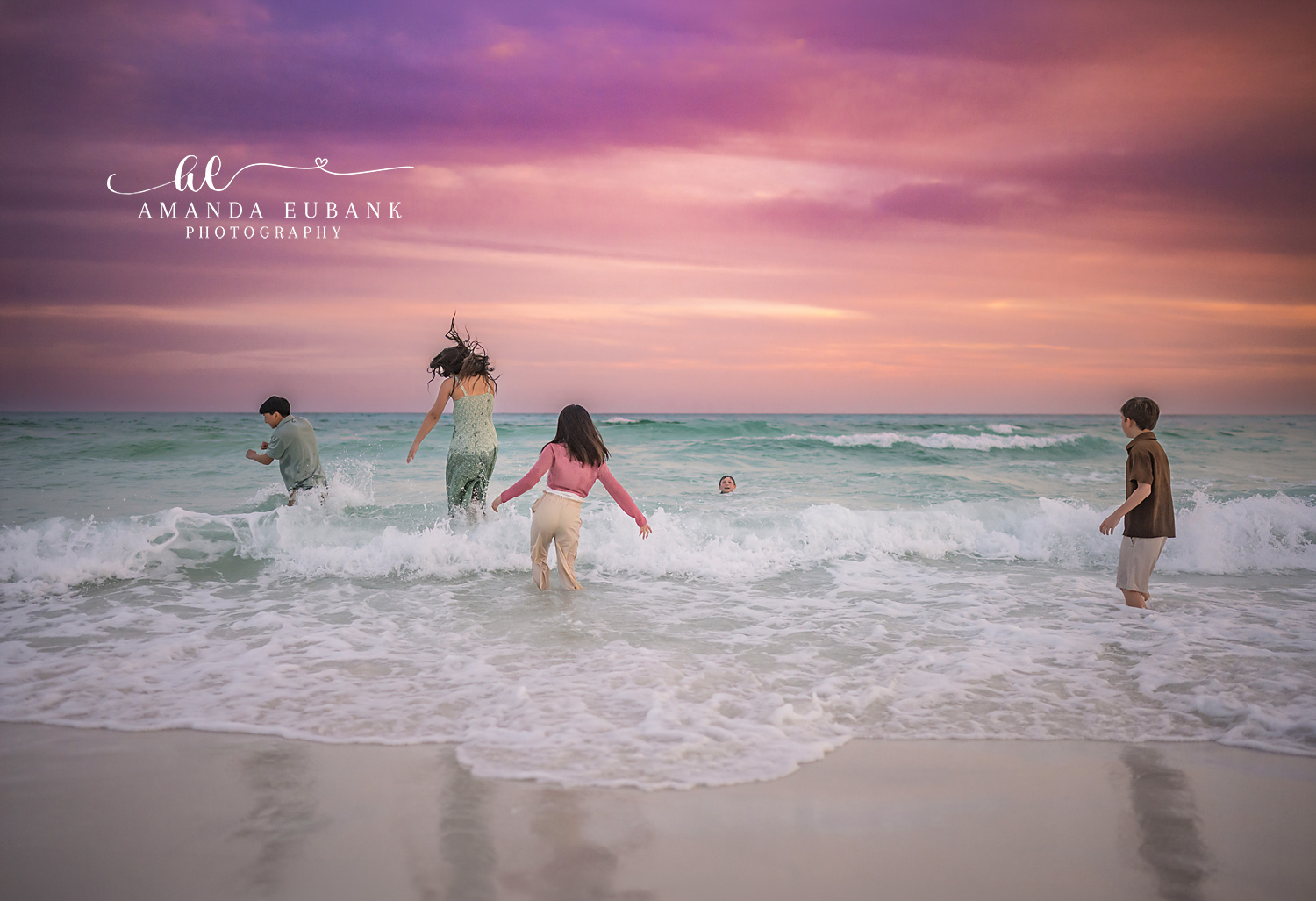 Miramar Beach Family Sunset Surf Play | Miramar Beach FL Family Photographer Family of four playing in the Gulf surf at sunset on Miramar Beach FL beneath a vivid purple, pink, and orange sky