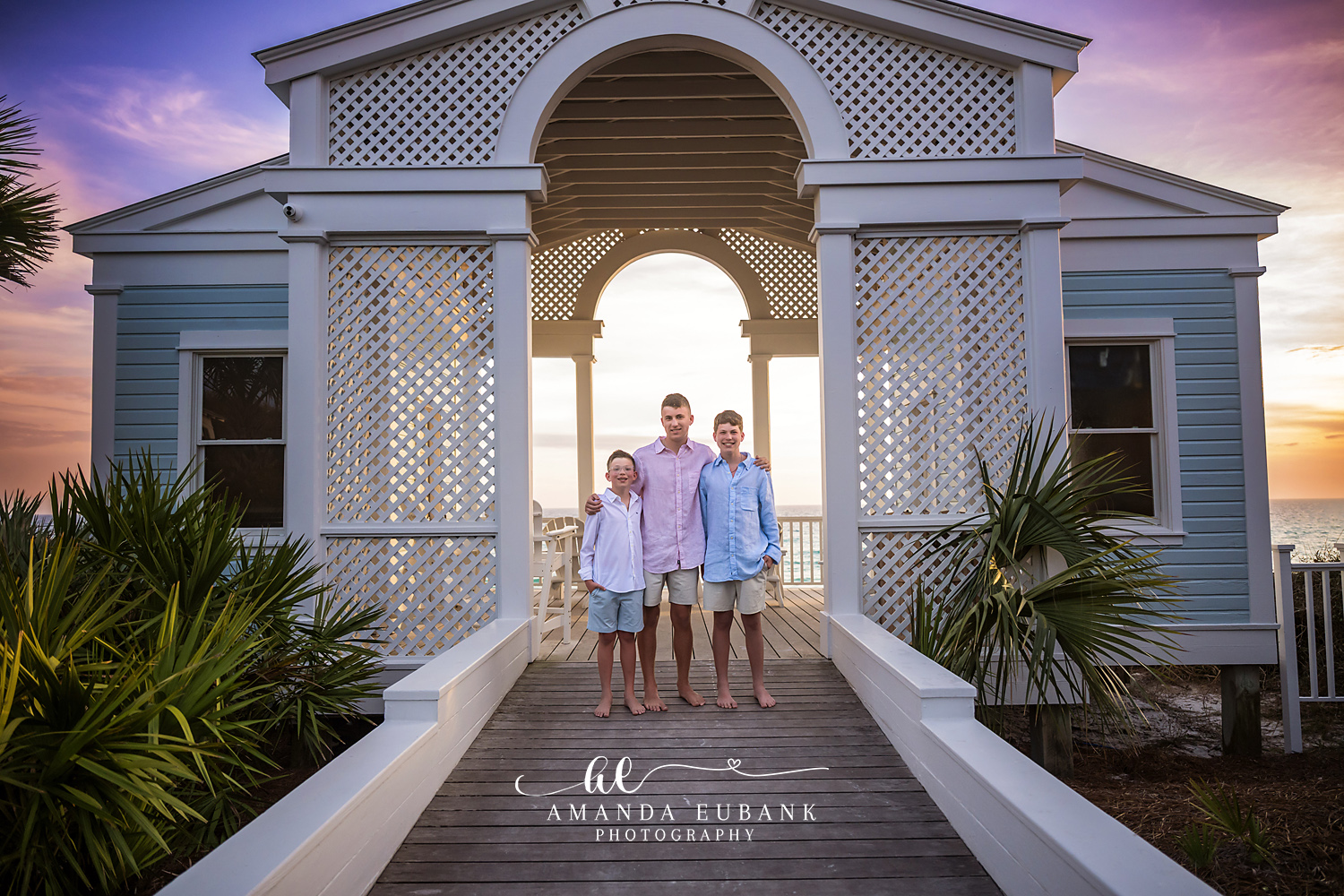 Seaside FL Brothers Portrait | Boardwalk Pavilion at Sunset Three brothers in pink and light blue button-ups standing barefoot under the white Seaside, FL pavilion as the sun sets behind them over the Gulf.