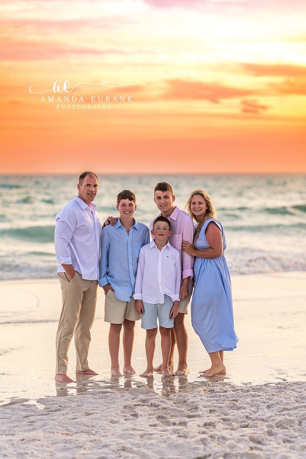 Seaside FL Family Portrait | Pastel Sunset on the Gulf Sand Vertical family of five portrait at the Seaside, FL shoreline beneath a soft peach and pink pastel sunset, family coordinated in pink, blue, and white linen.