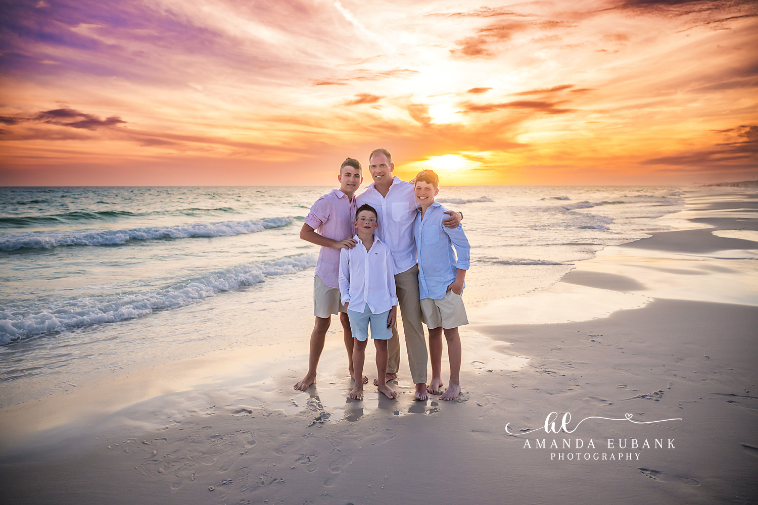 Seaside FL Father and Sons Sunset Portrait | Boys Beach Session Father in a white button-up surrounded by his three sons in pink, white, and light blue at the Seaside, FL surf line beneath a soft pastel orange and lavender sunset.