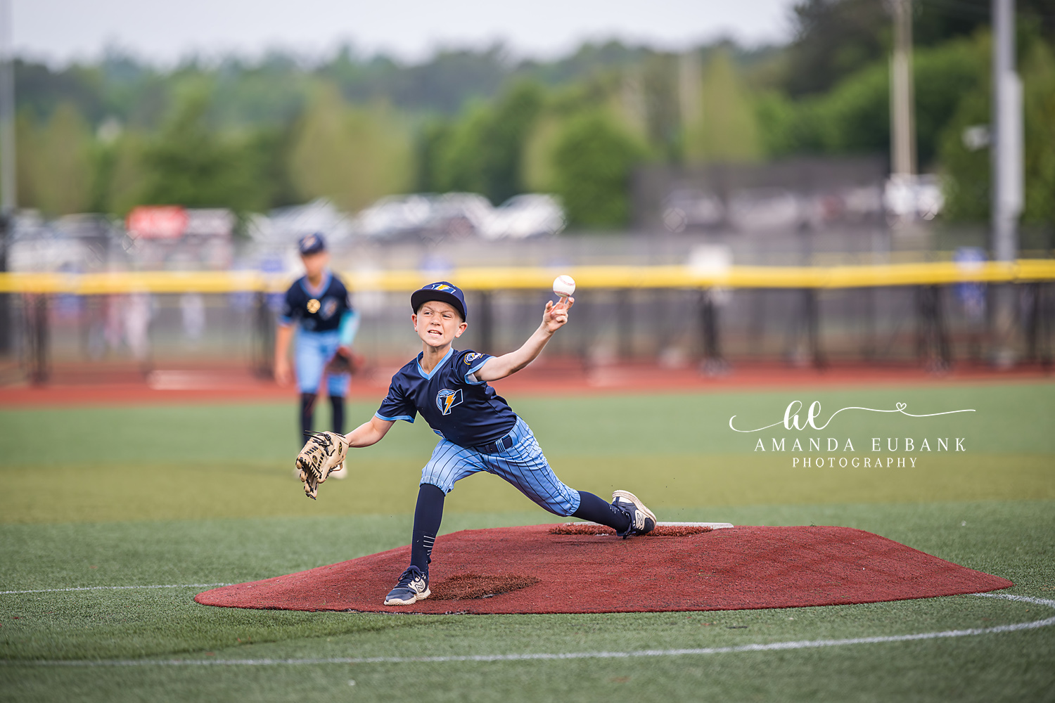 Pitcher Releasing Fastball | Hoover AL Travel Baseball Photographer Power Kilcrease 11U pitcher in navy and light blue pinstripe uniform follows through on a fastball release from the red clay mound during a Hoover, Alabama tournament game.