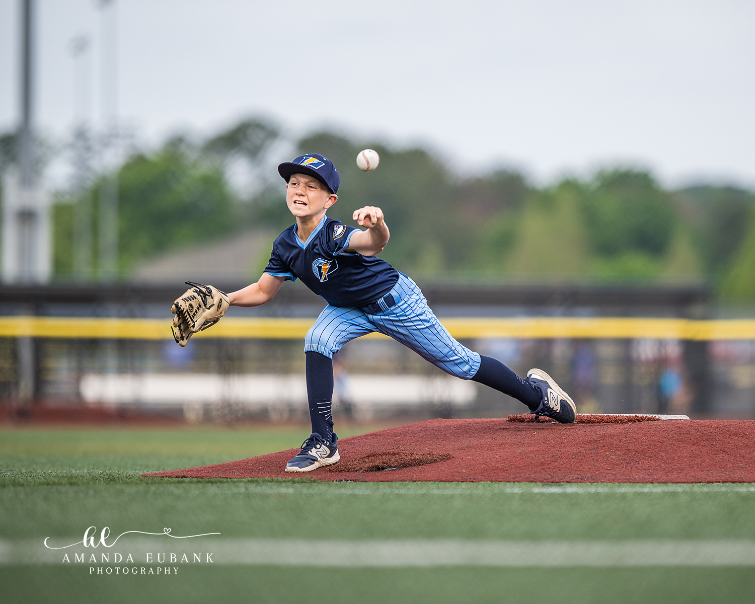 Pitcher Front Angle Release | Hoover AL Travel Baseball Photographer Power Kilcrease 11U pitcher releases the ball from the red dirt mound in a front-on view, navy jersey and light blue pinstripe pants standing out against the green field at a Hoover, Alabama tournament.