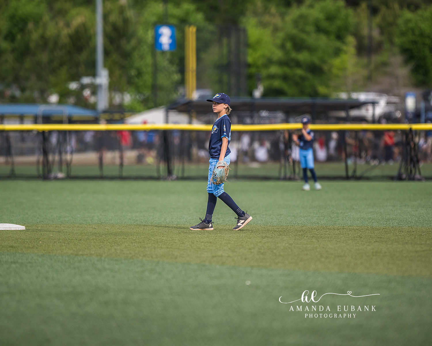 Outfielder Walking onto Field | Hoover AL Travel Baseball Photographer A Power Kilcrease 11U outfielder walks across the green grass with glove on hand, glancing back over his shoulder, with the Hoover Met tournament complex spread out behind him in Hoover, Alabama.