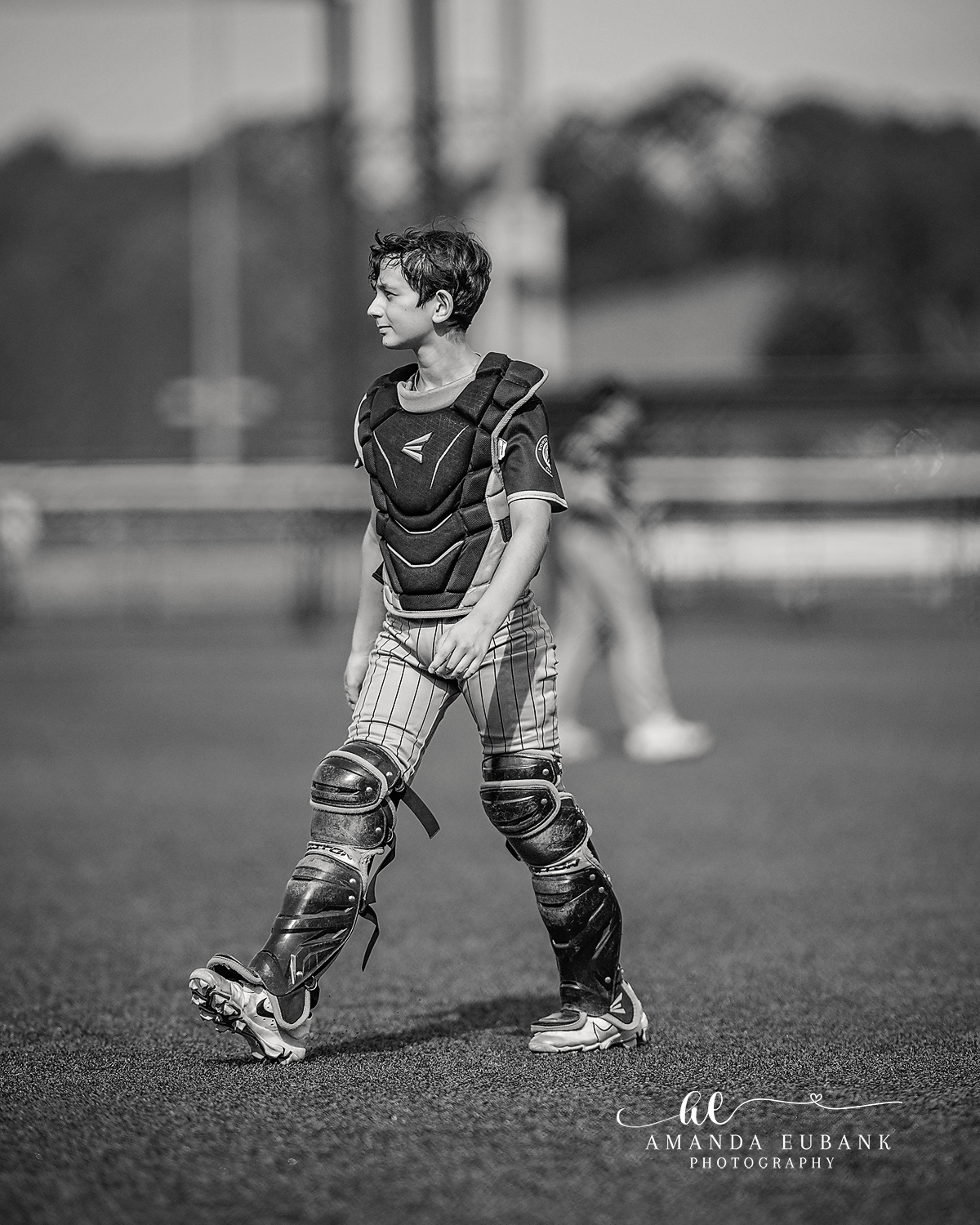 Catcher Walking Helmet Off | Hoover AL Travel Baseball Photographer Black and white walking portrait of a Power Kilcrease 11U catcher with chest protector and leg guards on but helmet off, striding across the field during a Hoover, Alabama tournament.