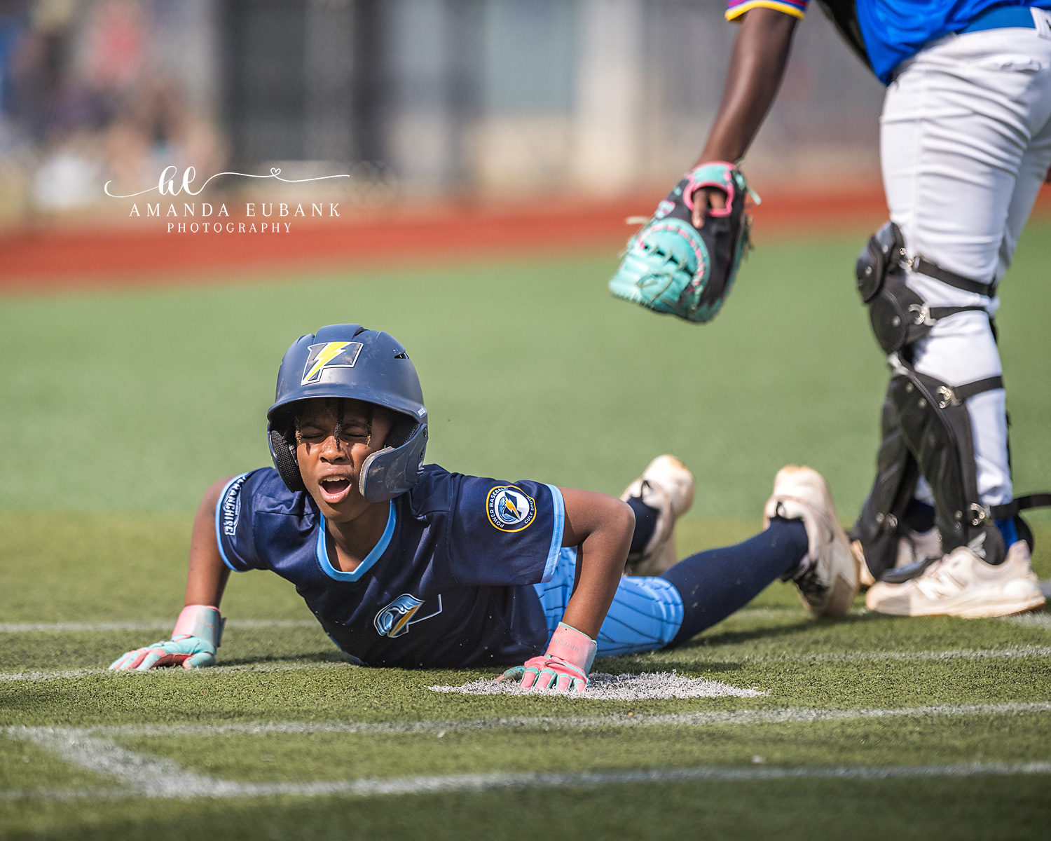 Headfirst Slide Safe Call | Hoover AL Travel Baseball Photographer Power Kilcrease 11U baserunner slides headfirst into the base with a fierce yell, hand grasping the bag in a cloud of chalk dust as the opposing catcher's teal mitt and leg guards loom above during a Hoover, Alabama tournament game.