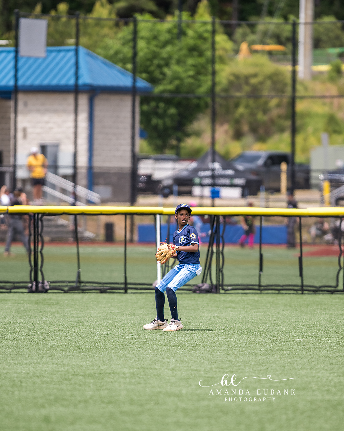 Outfielder Holding Ball | Hoover AL Travel Baseball Photographer Power Kilcrease 11U outfielder stands solo in the green outfield grass holding ball and glove, the Hoover Met tournament complex stretching out behind him during a tournament game in Hoover, Alabama.