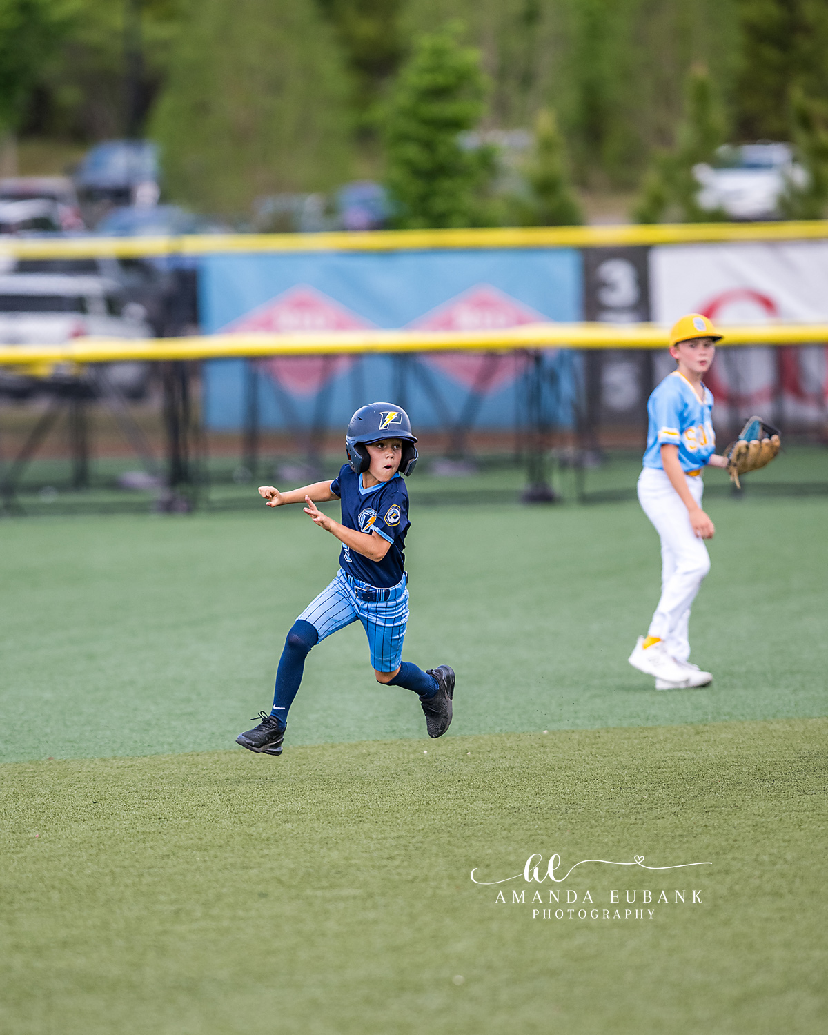 Baserunner Past Infielder | Hoover AL Travel Baseball Photographer Power Kilcrease 11U baserunner sprints past an opposing infielder during a Hoover, Alabama travel baseball tournament game with the yellow outfield wall and crowd behind.