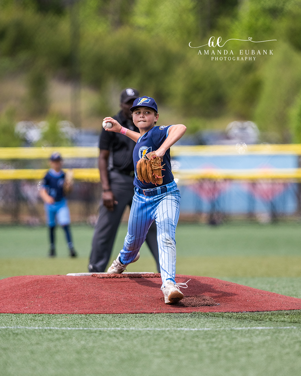 Pitcher Wind-Up Yellow P Cap | Hoover AL Travel Baseball Photographer Power Kilcrease 11U pitcher reaches the wind-up on the red dirt mound with the bright yellow Power P logo on his cap visible while the umpire watches from behind during a Hoover, Alabama tournament game.