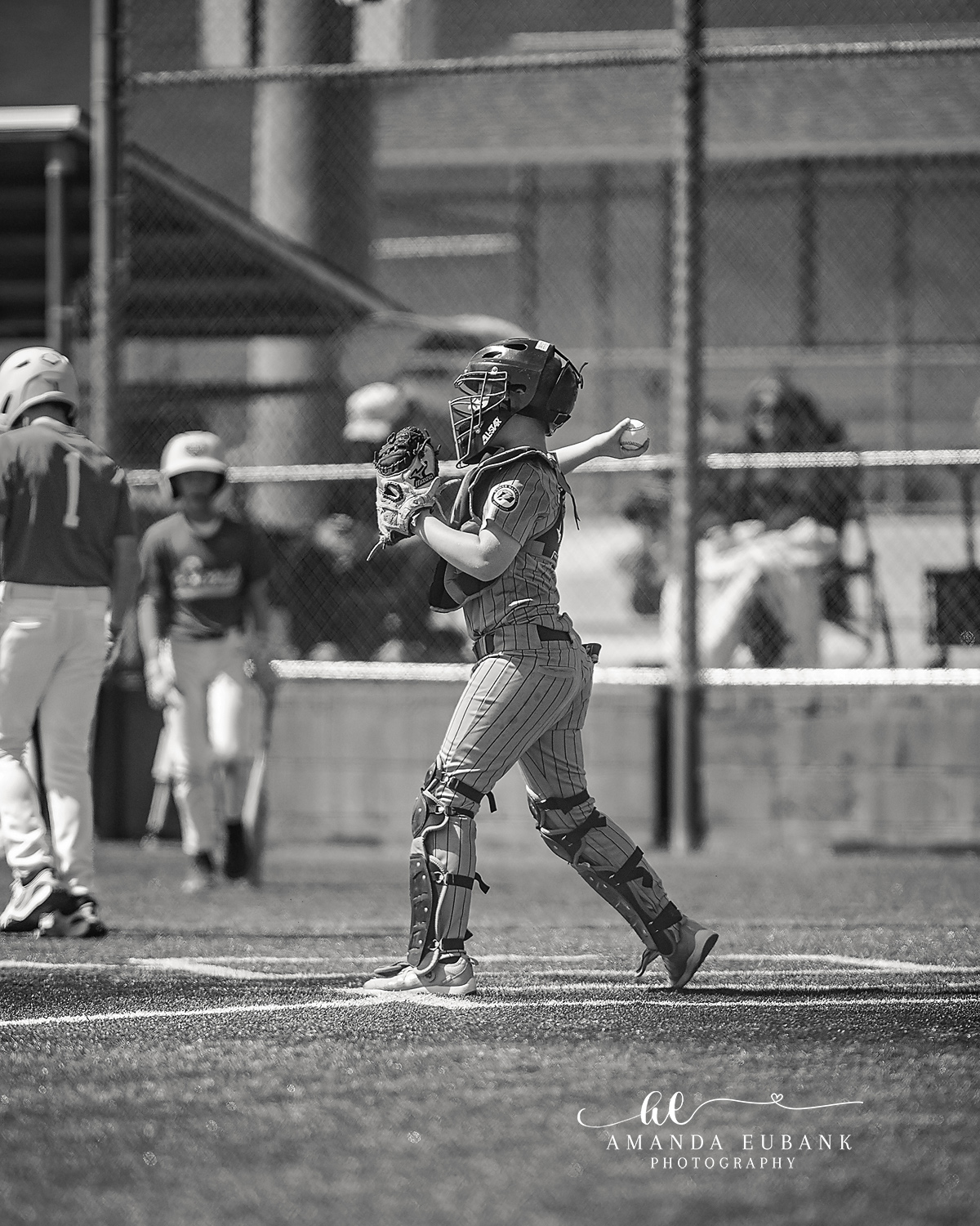 Catcher Throw Down BW | Hoover AL Travel Baseball Photographer Black and white image of a Power Kilcrease 11U catcher in full gear winding up to throw down to second base behind the chain-link backstop during a Hoover, Alabama tournament game.