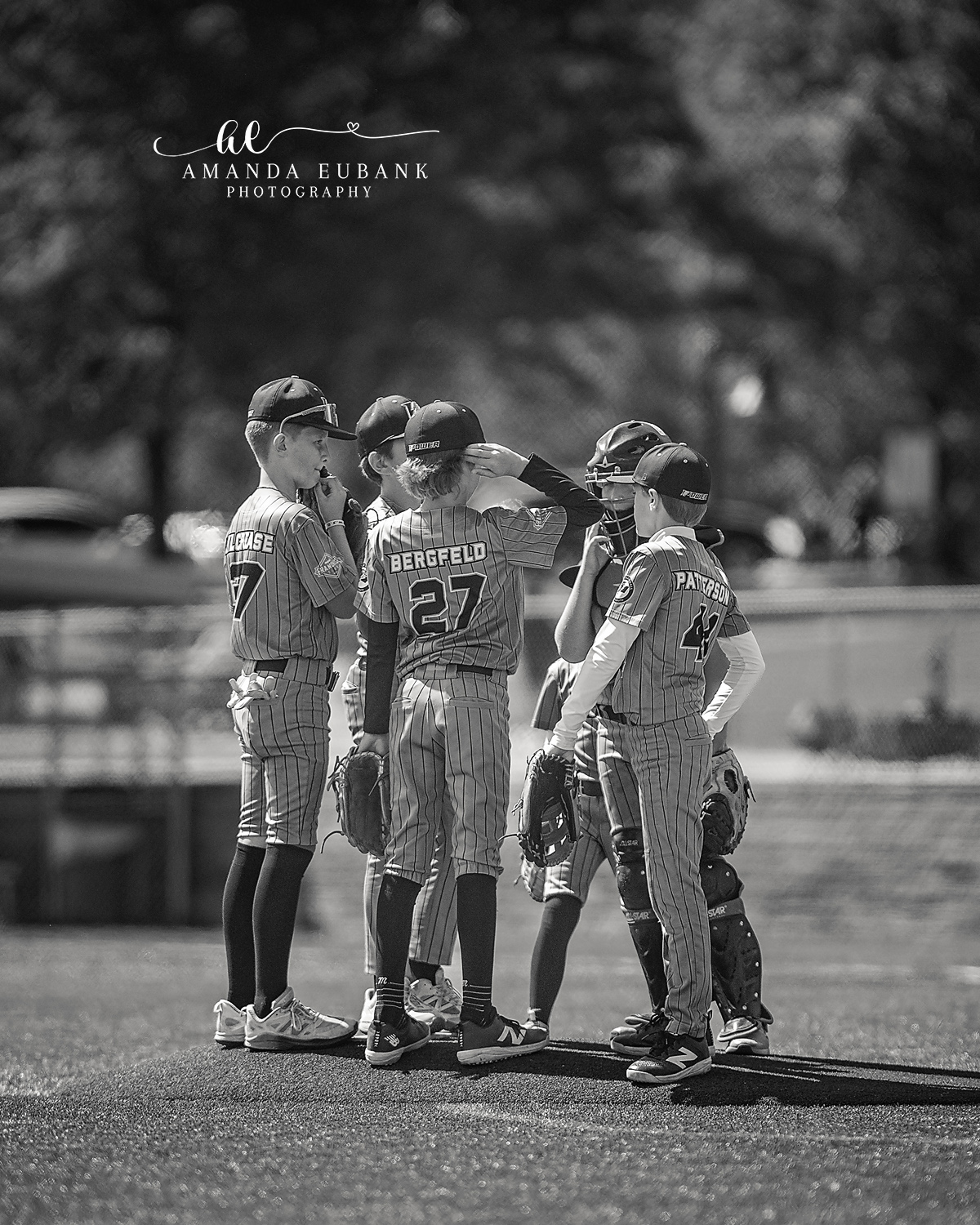 Player Huddle Strategy Talk BW | Hoover AL Travel Baseball Photographer Black and white image of five Power Kilcrease 11U players huddled together on the field — Cochran number 7, Bergfeld number 27, and Patterson among them — strategizing during a Hoover, Alabama tournament game.