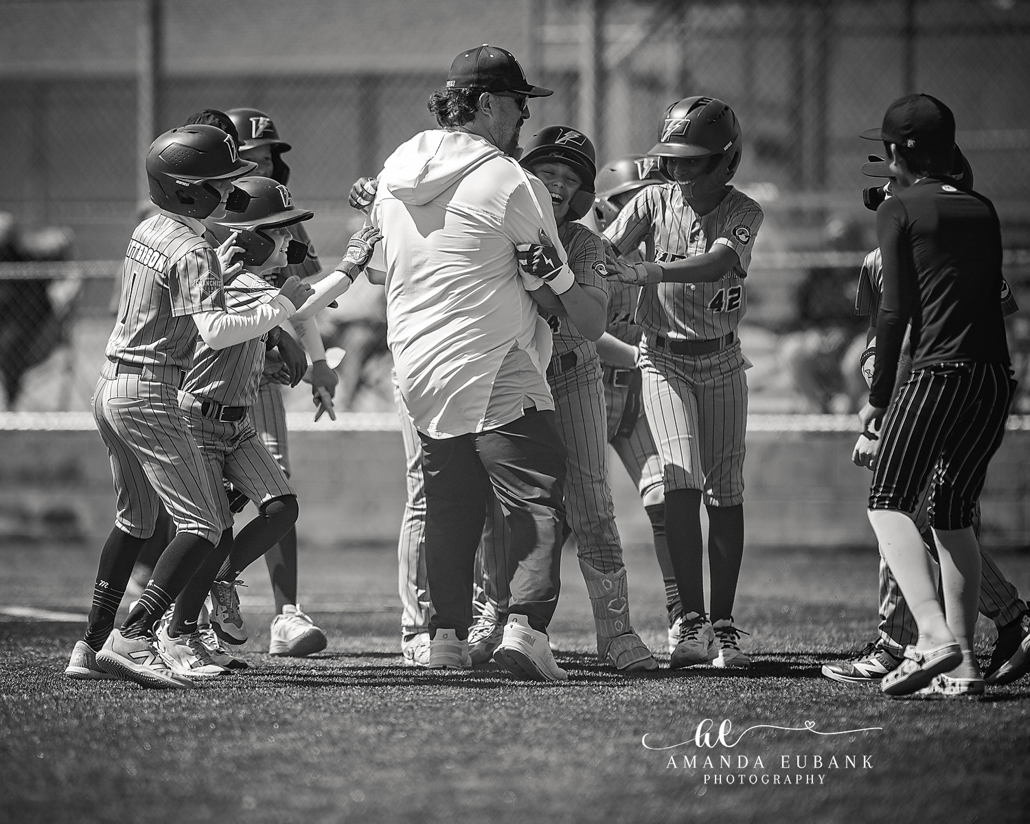 Team Celebration Mob BW | Hoover AL Travel Baseball Photographer Black and white image of Power Kilcrease 11U teammates and their coach mobbing a celebrating player in jersey number 42 after a big play during a Hoover, Alabama tournament game.