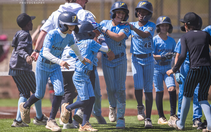 Smiling Power Kilcrease 11U players in light blue Power jerseys and pinstripe pants celebrate together on the infield, jersey number 42 at the center, during a Hoover, Alabama tournament game.