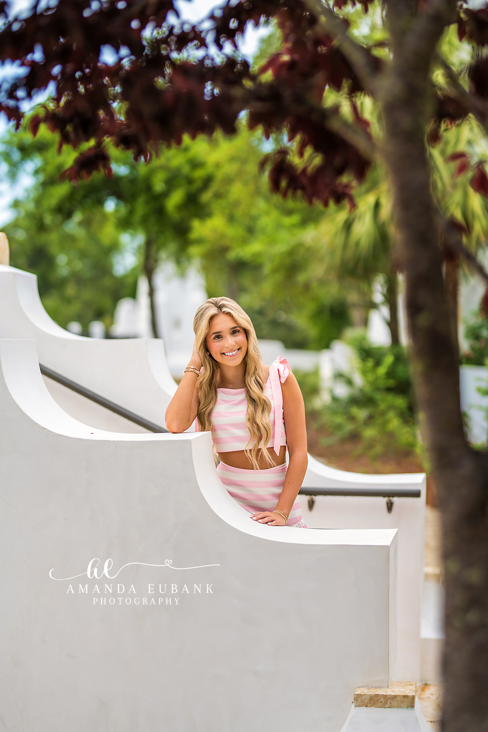 Curved White Bench Senior Portrait | Alys Beach Photographer Senior in a pink-striped two-piece on a curved white Alys Beach bench with tropical foliage, by Alys Beach Photographer Amanda Eubank.