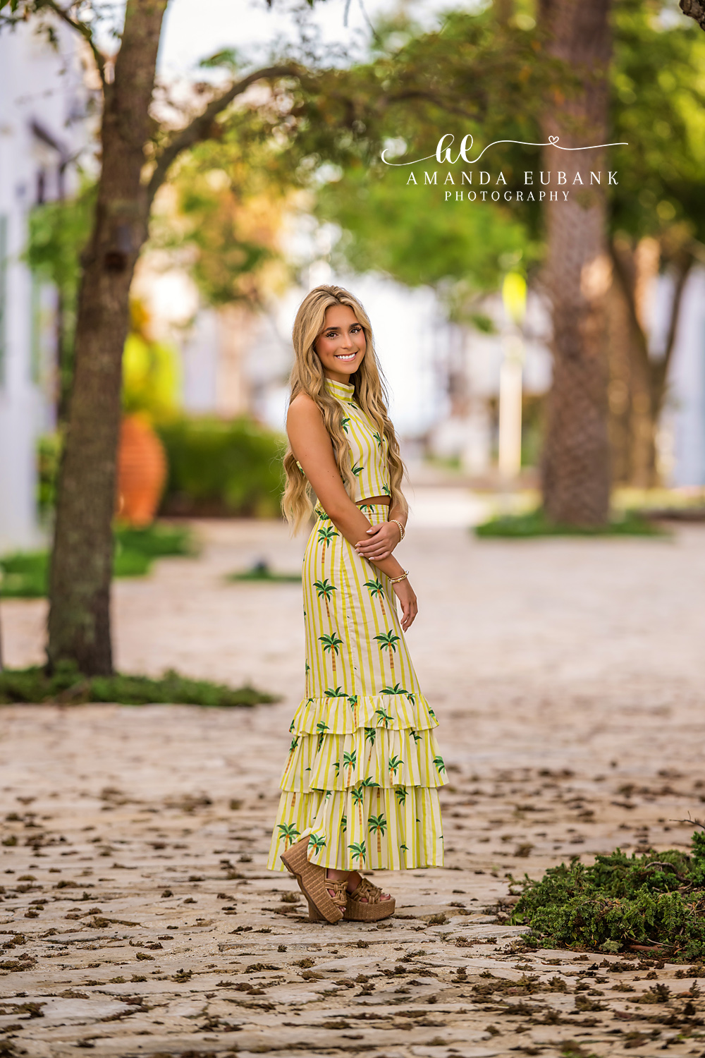 Senior Portrait in Palm-Print Set Among the Palms | Senior Photographer in Alys Beach Senior in a yellow palm-tree-print two-piece set on a shaded brick path lined with palms, by Senior Photographer in Alys Beach Amanda Eubank.