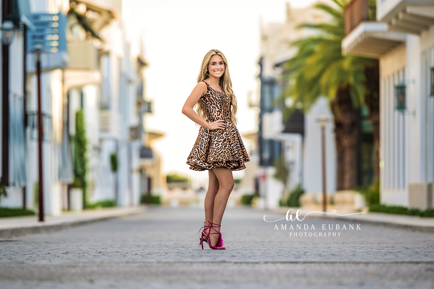 Senior Style on Alys Beach Street | Photographer in Alys Beach Senior in a leopard mini dress posing on a brick Alys Beach street with palms and white architecture, by Photographer in Alys Beach Amanda Eubank.