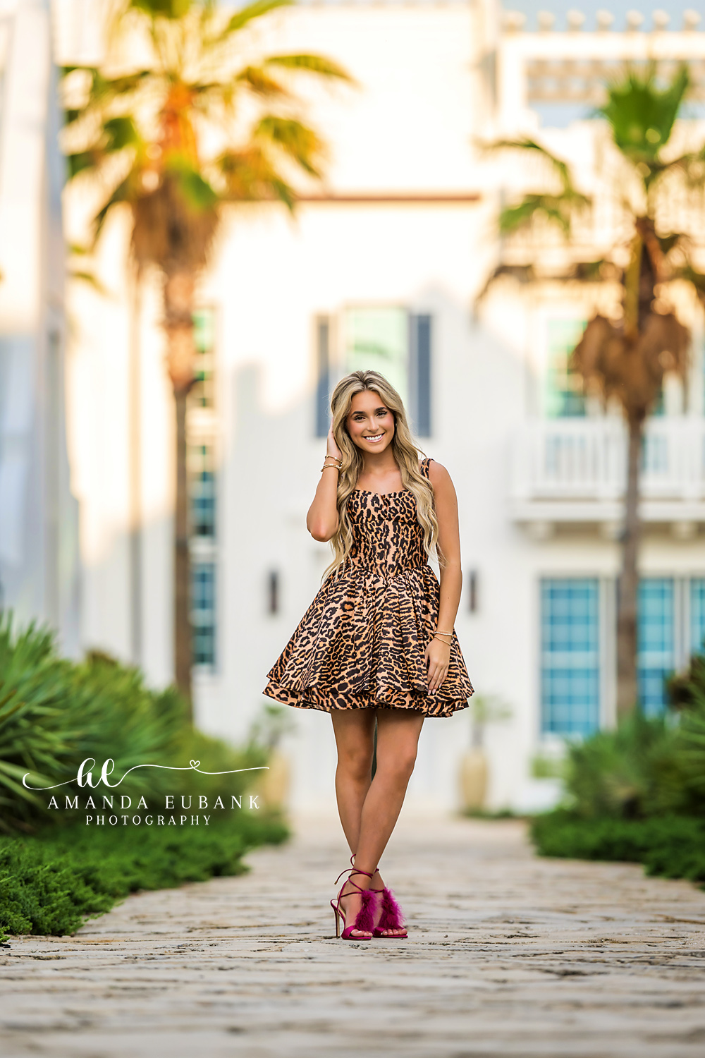 Editorial Senior Style in Alys Beach | Senior Photographer in Alys Beach Senior in a leopard mini dress and fuchsia heels walking through Alys Beach palms and white architecture, by Senior Photographer in Alys Beach Amanda Eubank.