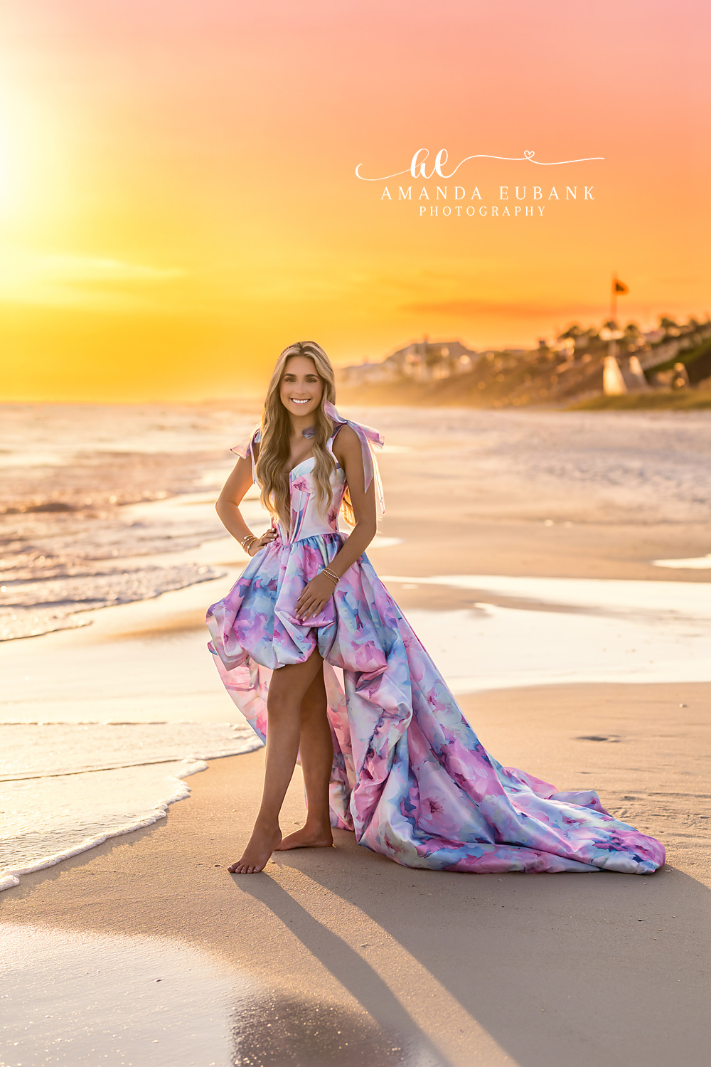 Golden Sunset Senior Portrait with Alys Beach Skyline | Alys Beach Photographer Senior in a pastel watercolor high-low gown standing barefoot on the sand at golden sunset with the Alys Beach skyline behind her, by Alys Beach Photographer Amanda Eubank.