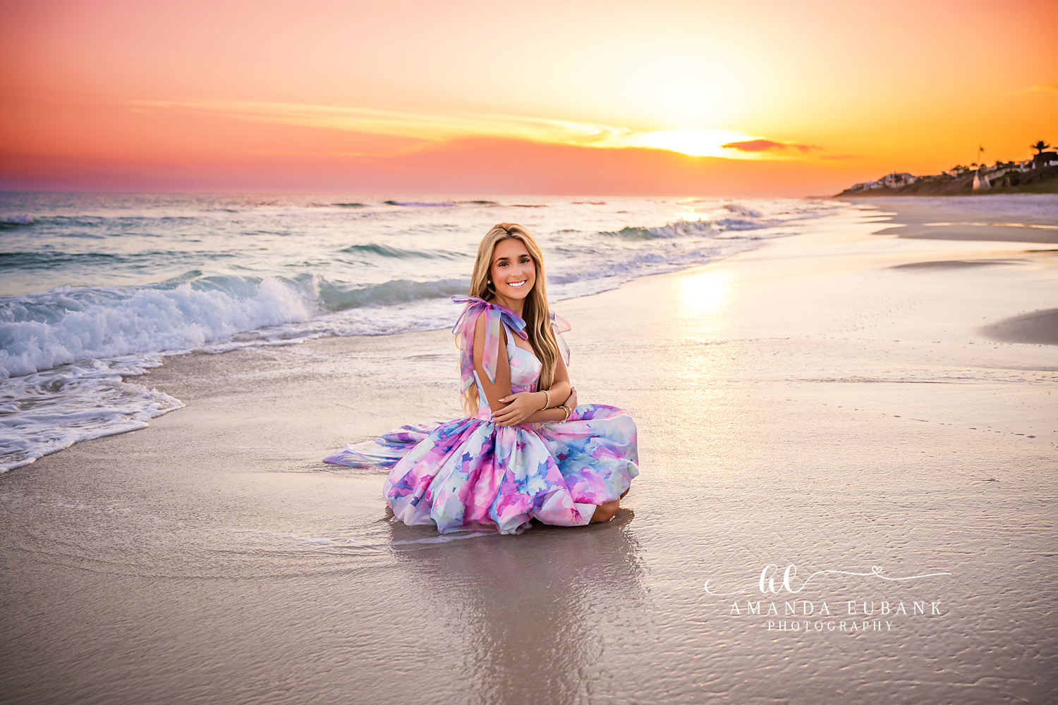 Sunset Coastline Senior Session | Senior Photographer in Alys Beach Senior girl kneeling on the wet sand at sunset with the coastline behind her, captured by Senior Photographer in Alys Beach Amanda Eubank.