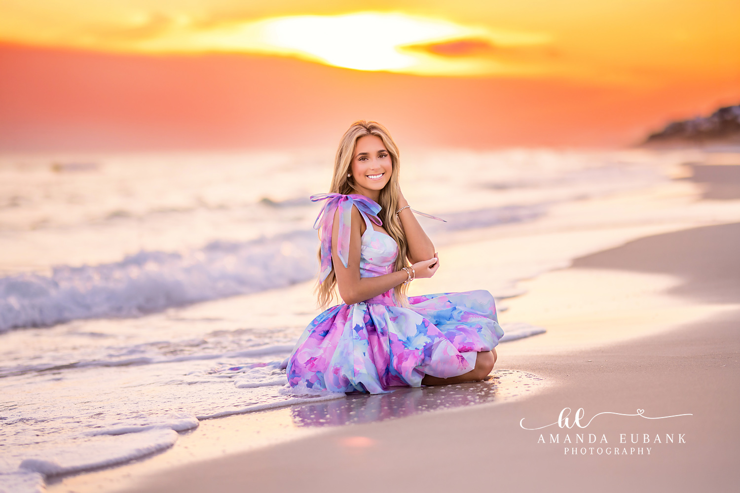 Sunset Beach Senior Portrait in Watercolor Gown | Photographer in Alys Beach Senior in a pastel watercolor-print gown kneeling at the shoreline under a fiery sunset, by Photographer in Alys Beach Amanda Eubank.