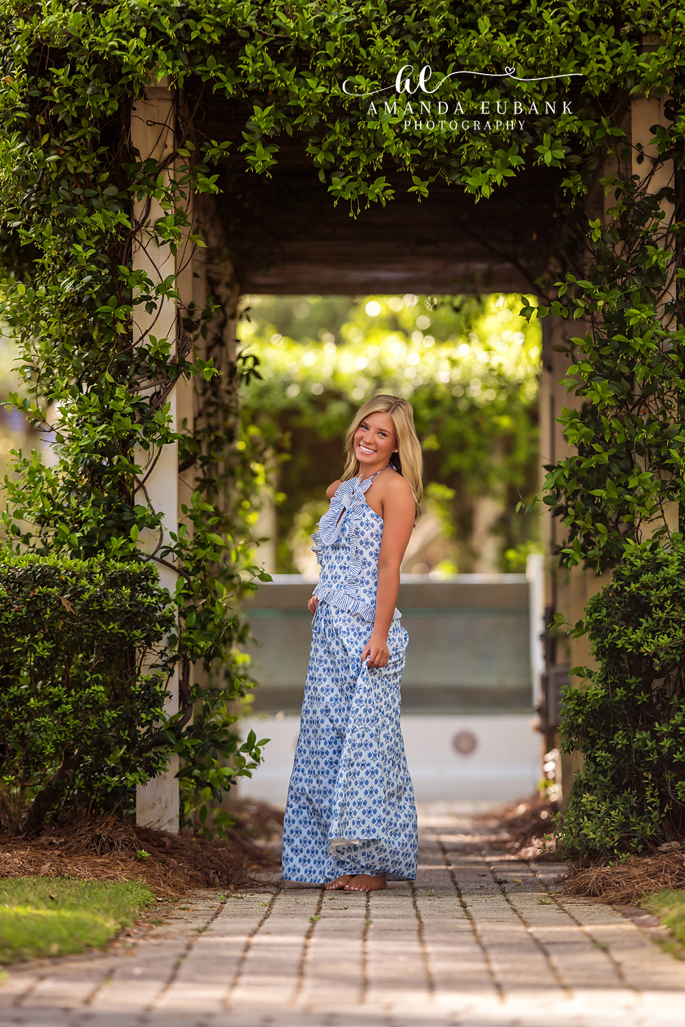 Rosemary Beach Vine Archway Senior Portrait | 30A Senior Photographer Senior girl in a blue and white halter maxi dress smiling inside a vine-covered archway in Rosemary Beach FL